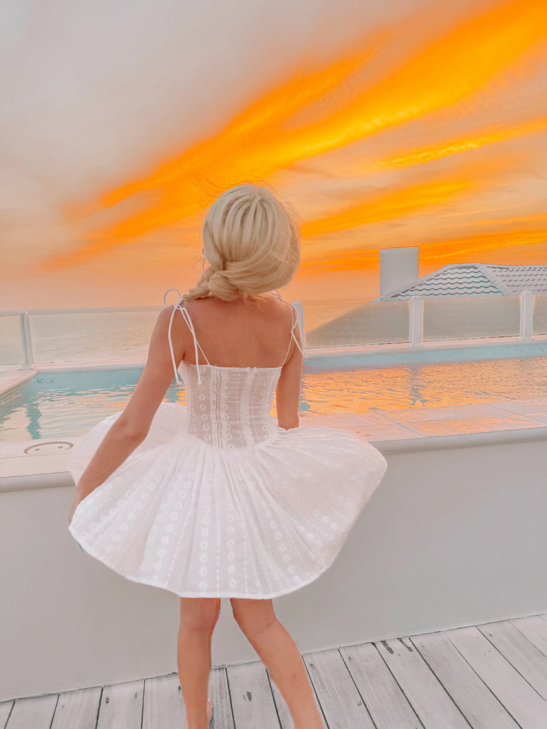 White eyelet mini dress by the pool at sunset.
