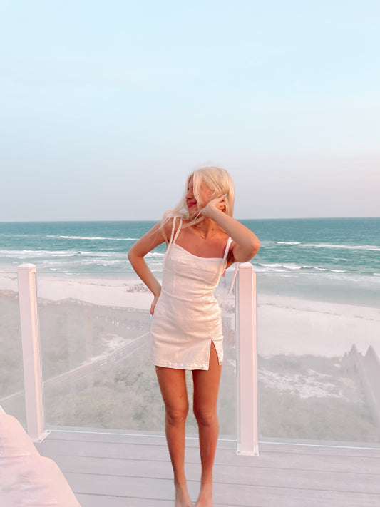 Off-white mini dress on a beachside deck, ocean view.
