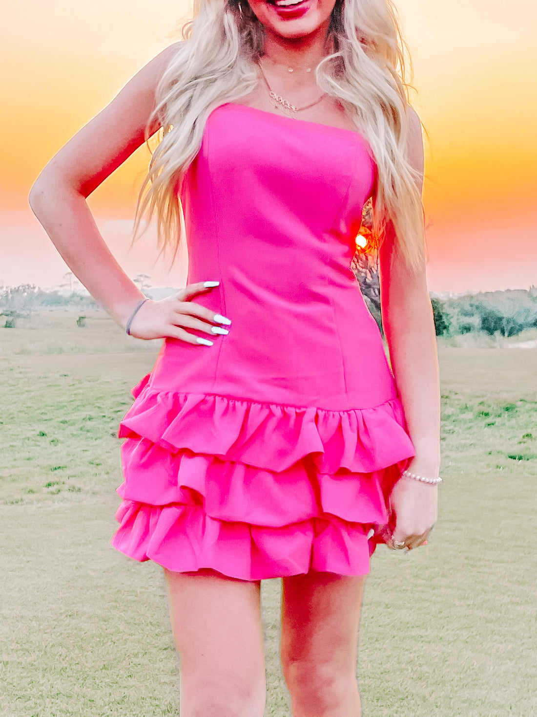 Pink strapless mini dress with tiered ruffles, shown outdoors at sunset.
