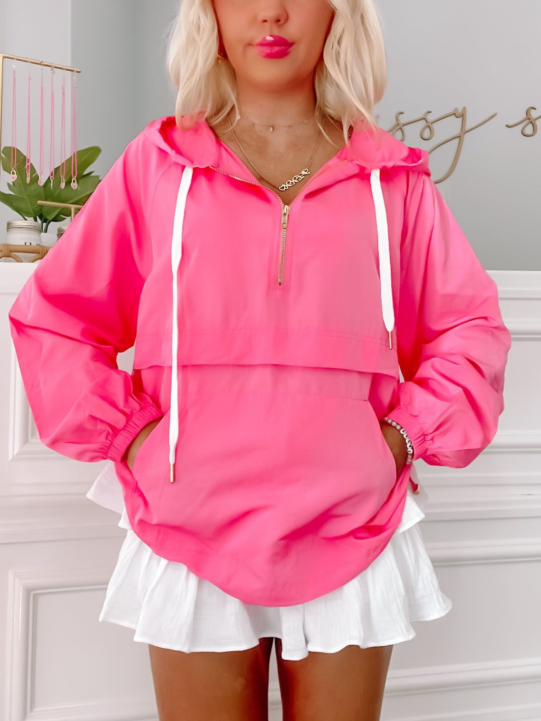 Hot pink windbreaker with white drawstring and pockets, modeled over white pleated skirt.
