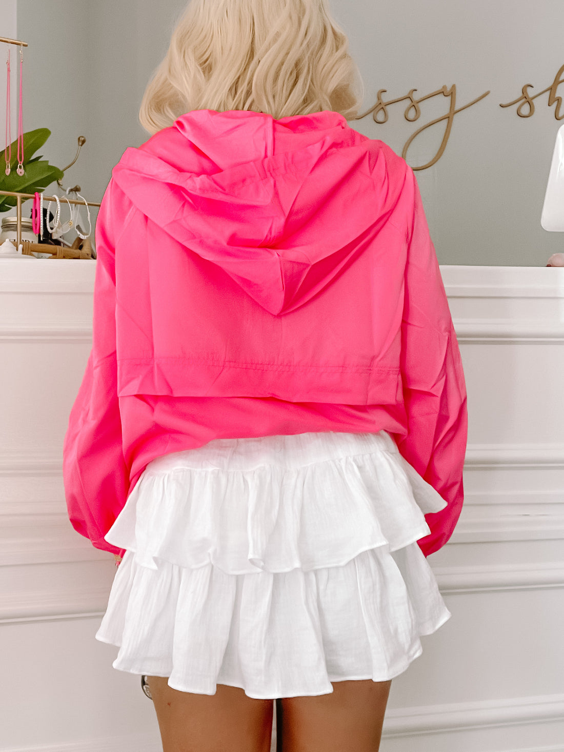 Bright pink hooded jacket paired with a white ruffled mini skirt, shown from the back.
