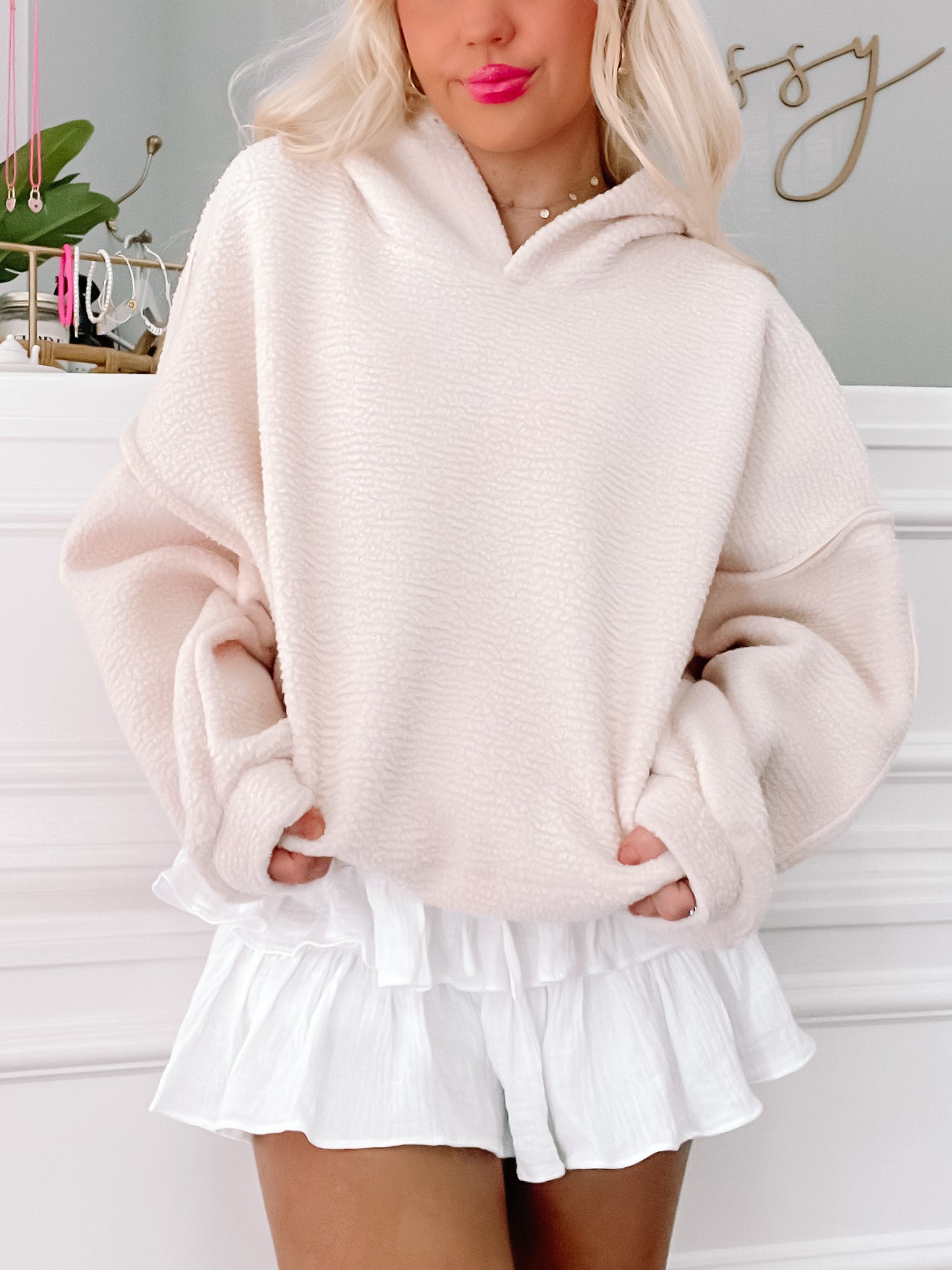 Cream-colored fleece pullover, oversized fit, modeled with white ruffled shorts.
