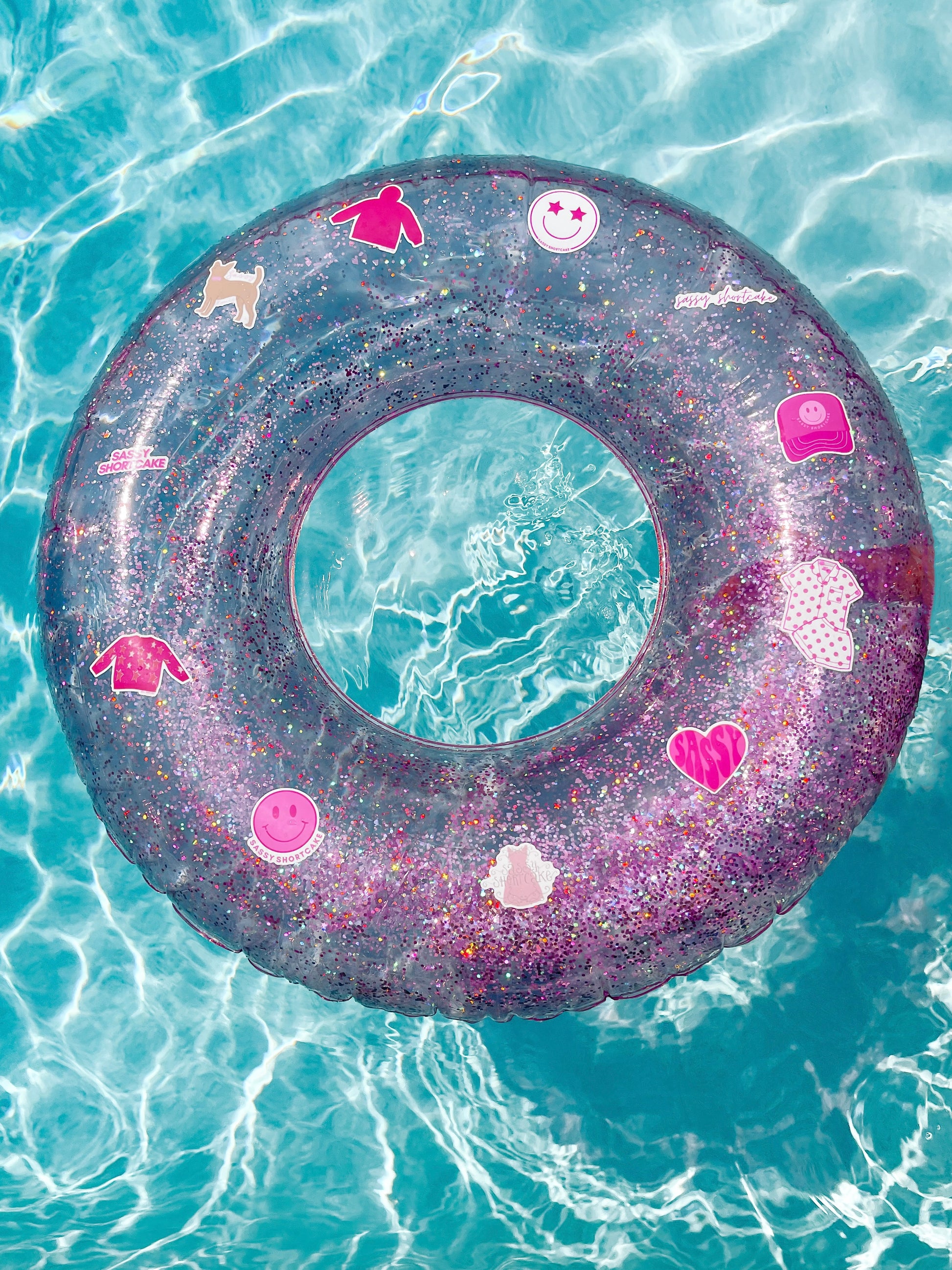Pink glitter pool float with assorted stickers, floating in a turquoise pool.
