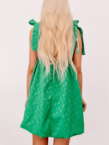 Emerald green mini dress with tie straps, shown from the back on a model.
