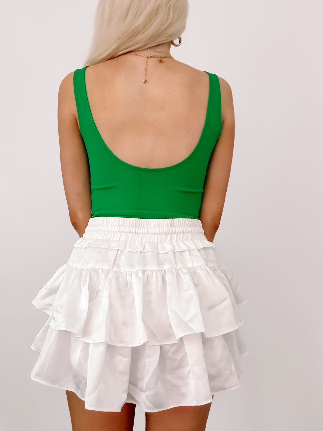 Kelly green bodysuit and white tiered ruffle mini skirt against a white backdrop.
