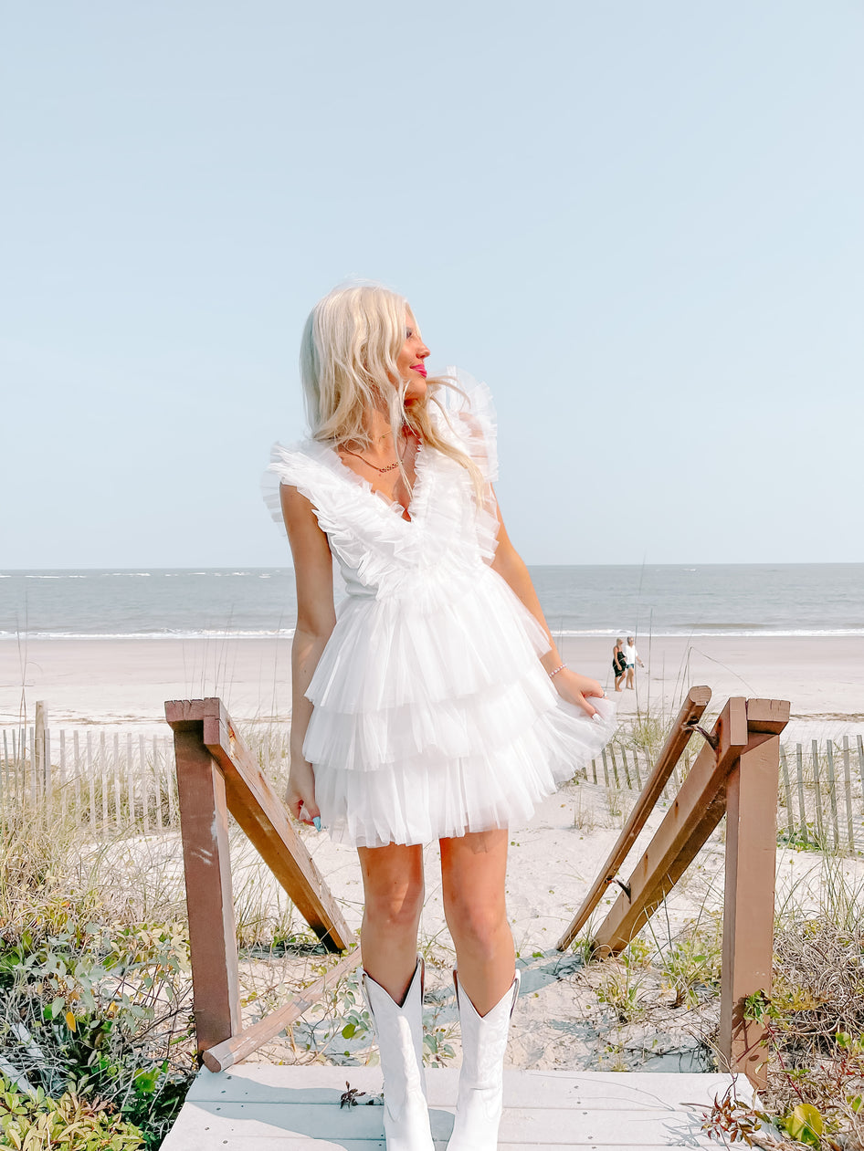 White tiered tulle dress styled at the beach; woman in white cowboy boots.
