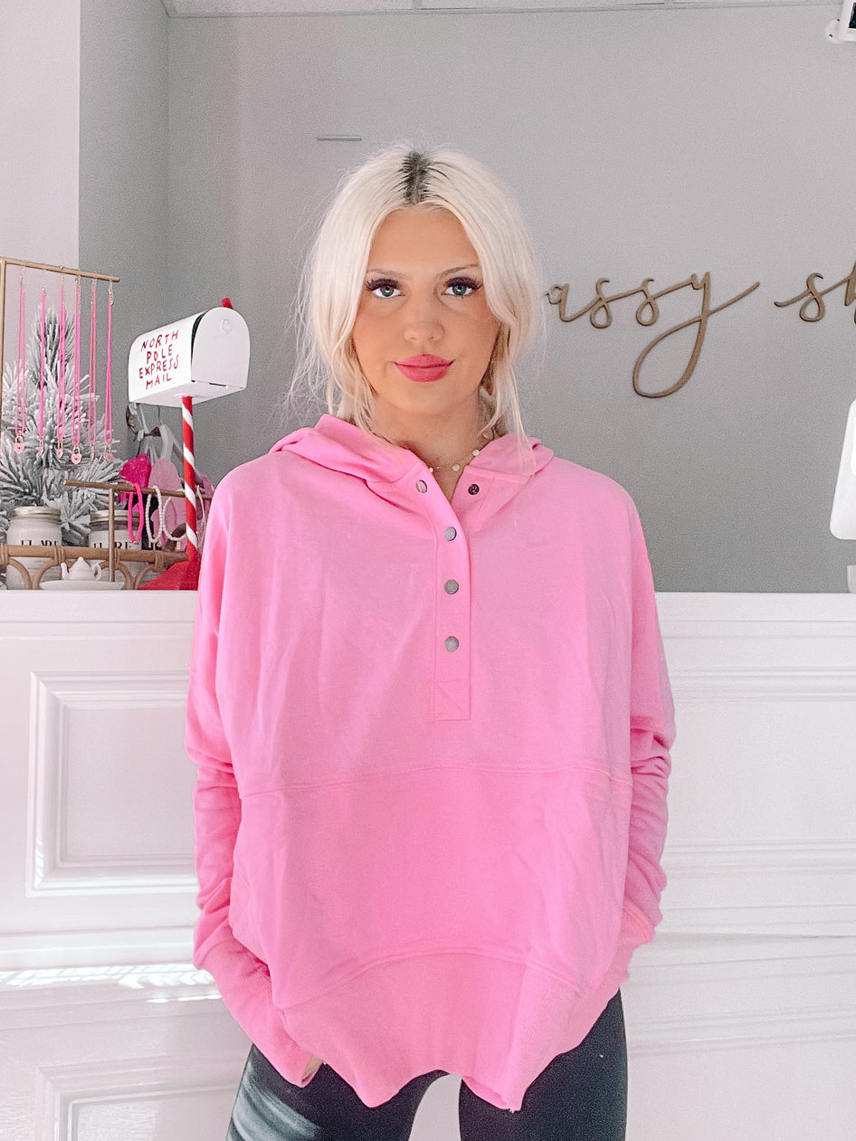 Bubblegum pink pullover hoodie with button placket, modeled against a gray wall.
