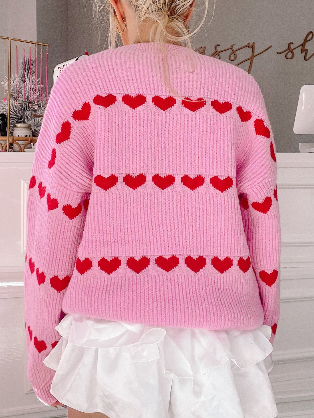 Pink knit sweater with red heart details, shown from the back.
