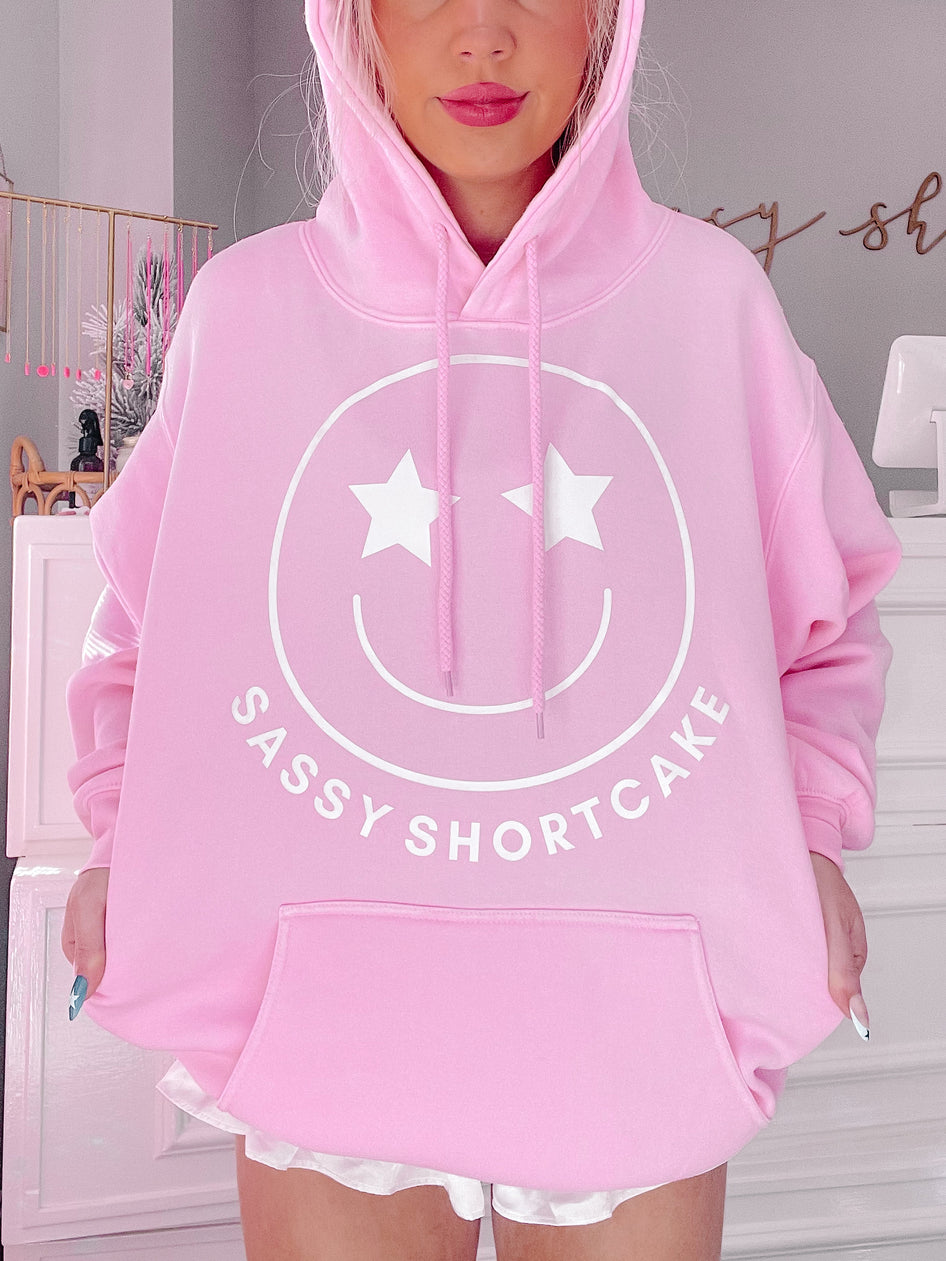 Pink hoodie featuring a smiling face graphic and "Sassy Shortcake" text.
