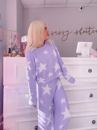 Lilac star-print pajama set, cozy knit fabric, worn by a model in a boutique.
