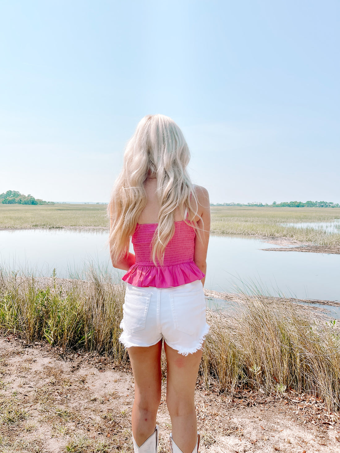 Woman in pink crop top and white denim shorts by tranquil marsh.
