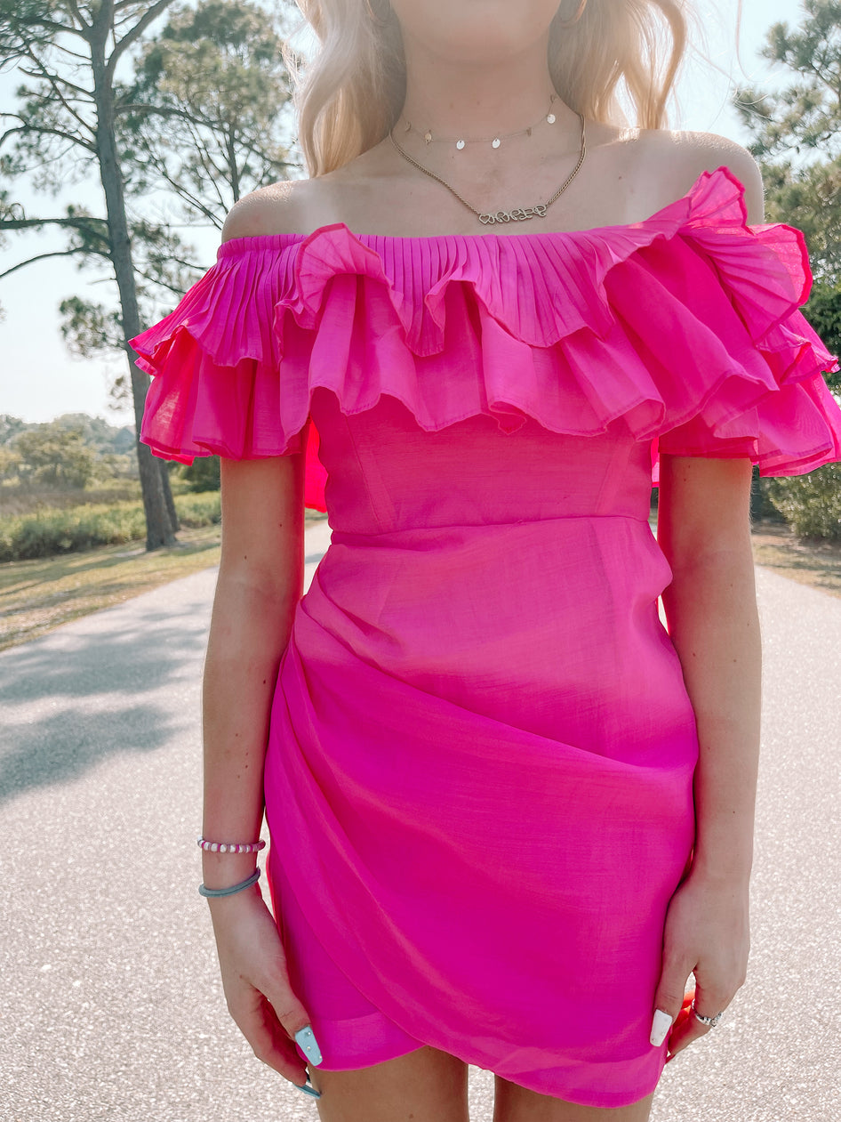 Hot pink off-the-shoulder mini dress, pleated bodice, outdoors.
