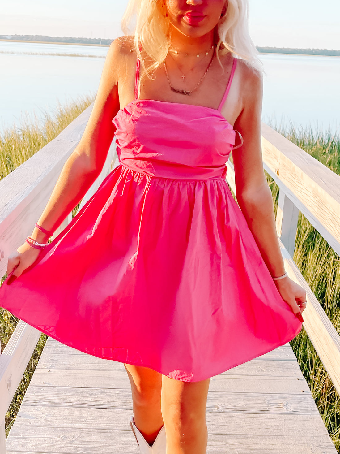 Hot pink sundress on a boardwalk overlooking a tranquil waterfront.
