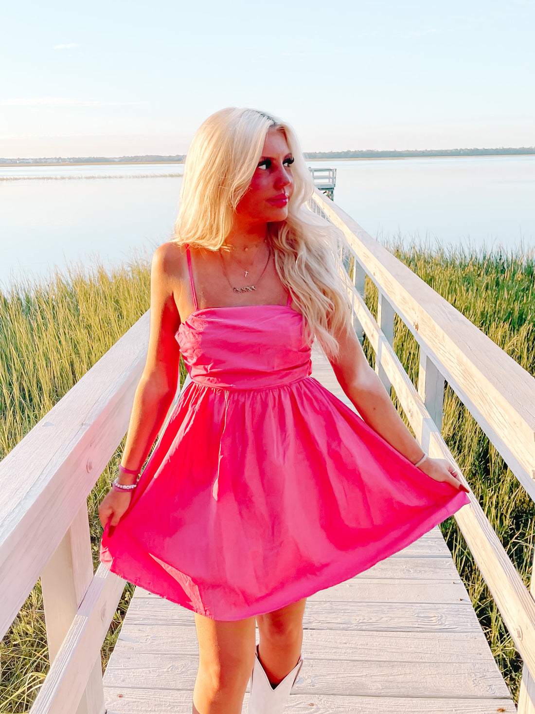 Hot pink sundress on a boardwalk overlooking a tranquil waterfront.
