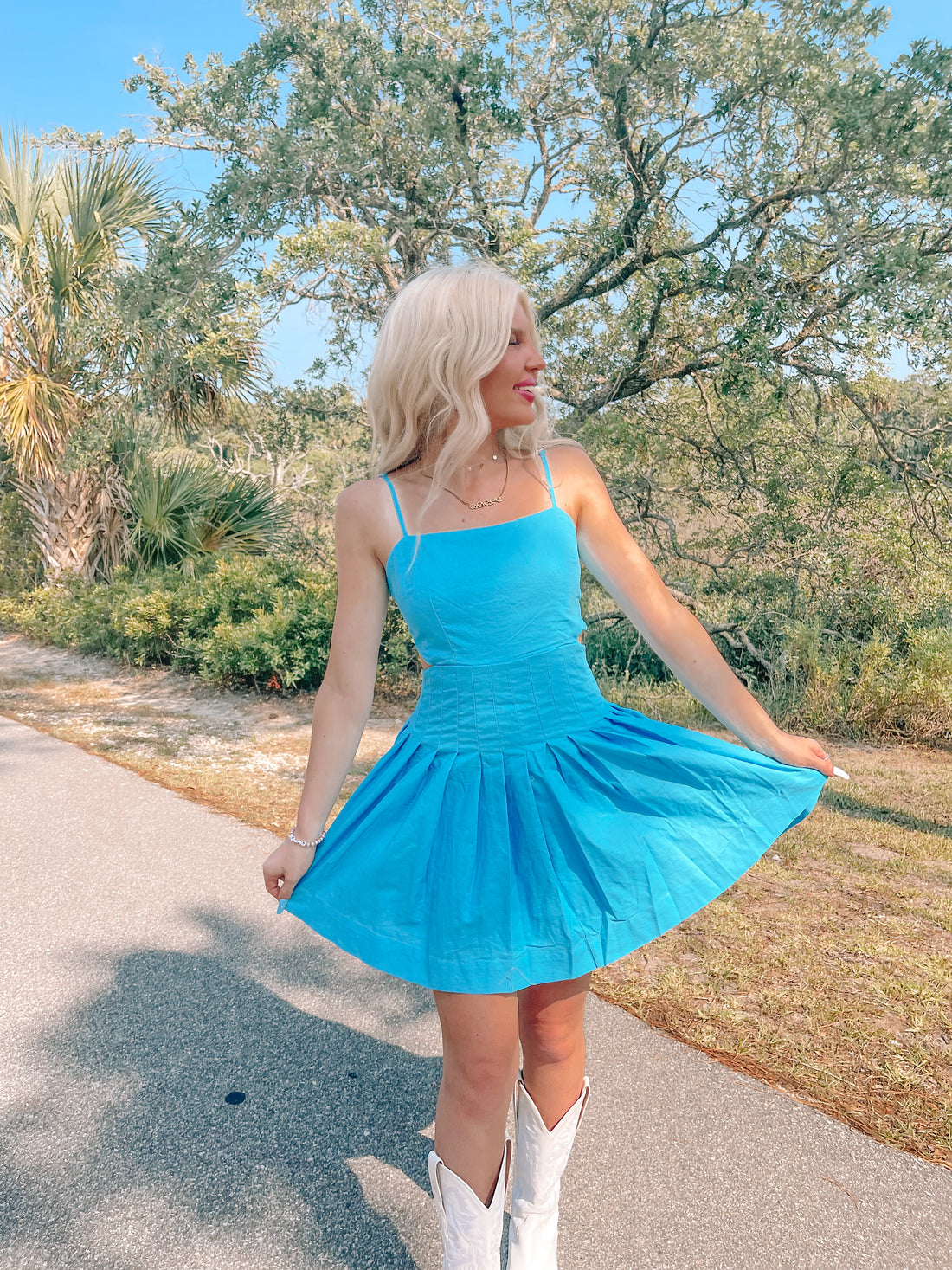 Bright blue pleated mini dress outdoors, styled with white cowboy boots.
