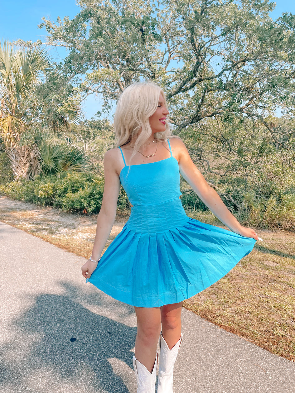 Bright blue pleated mini dress outdoors, styled with white cowboy boots.

