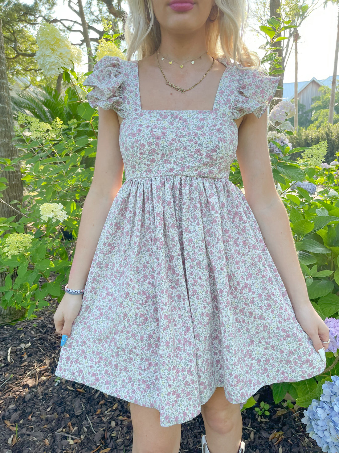 Floral mini dress with ruffled sleeves, modeled outdoors amongst blooming hydrangeas.
