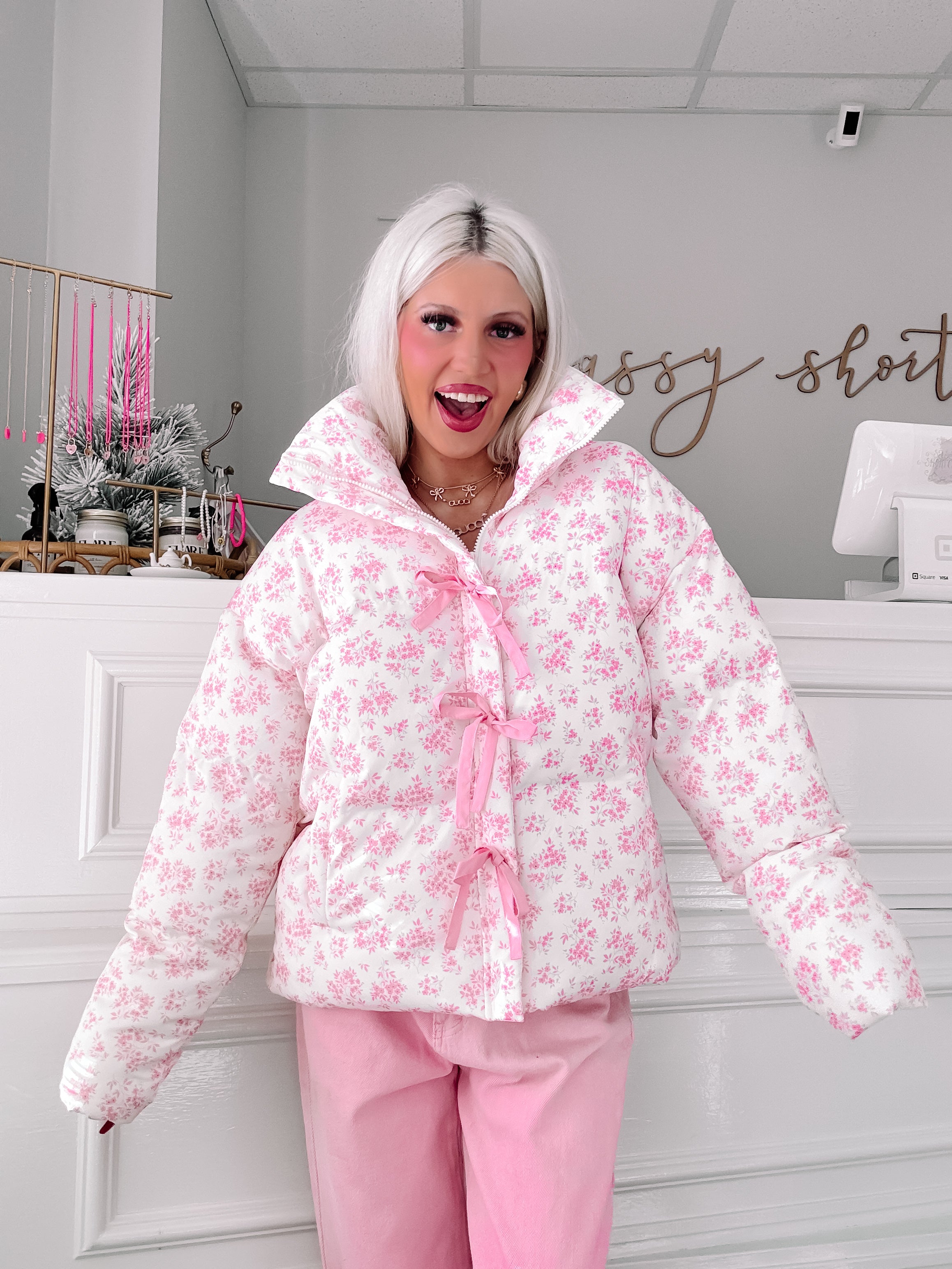 Pink floral puffer jacket with ribbon detailing, modeled in a boutique setting.
