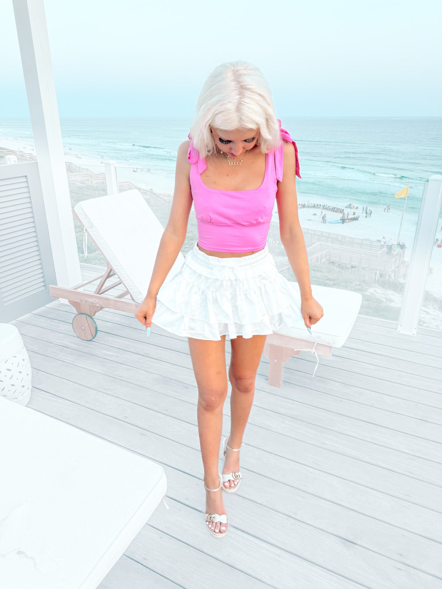 Woman in pink top and white ruffled skirt on a deck overlooking the ocean.
