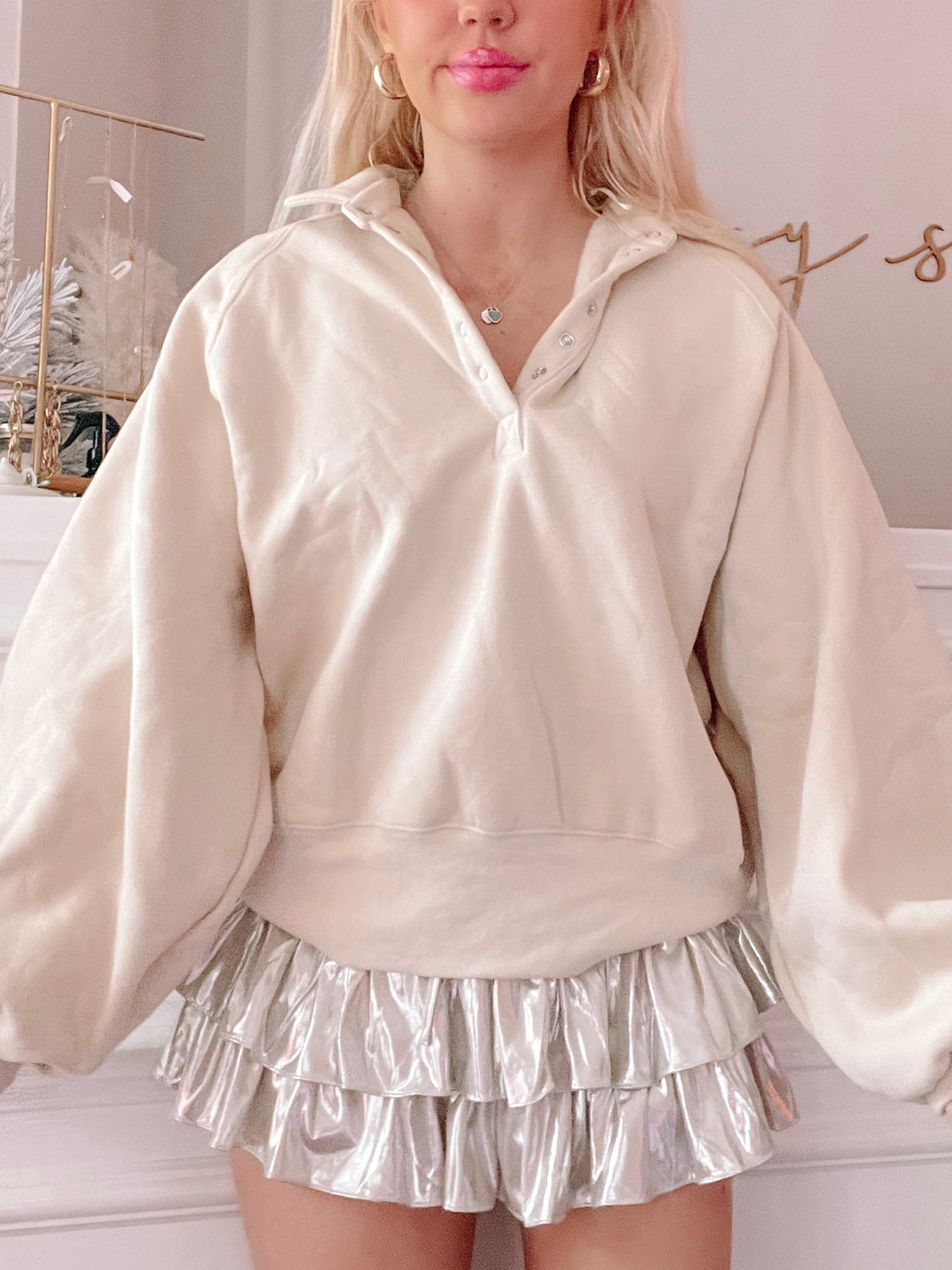 Cream-colored oversized pullover with button placket, styled with a shimmering silver ruffle skirt.
