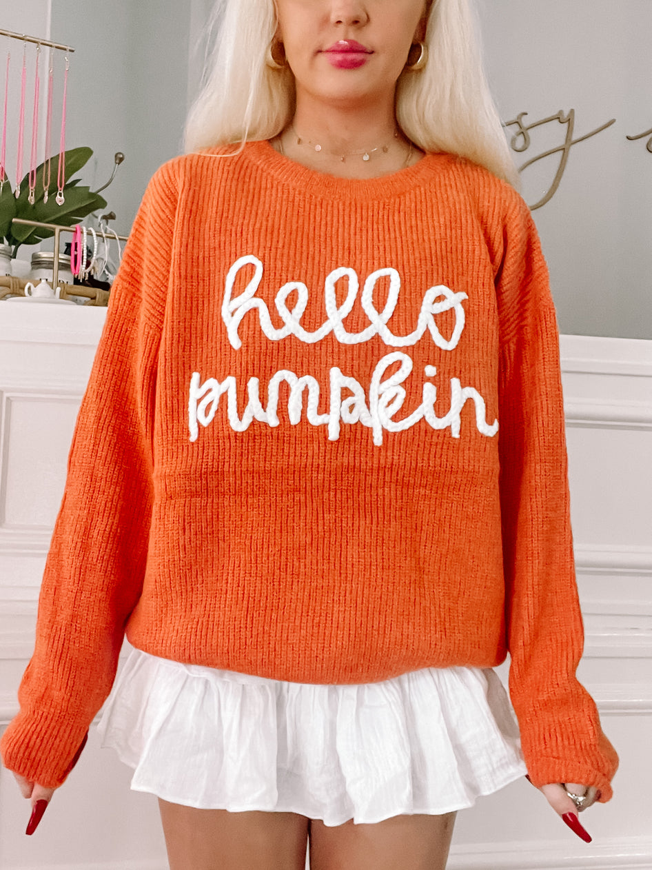 Orange knit sweater featuring "Hello Pumpkin" in white lettering; fall fashion.
