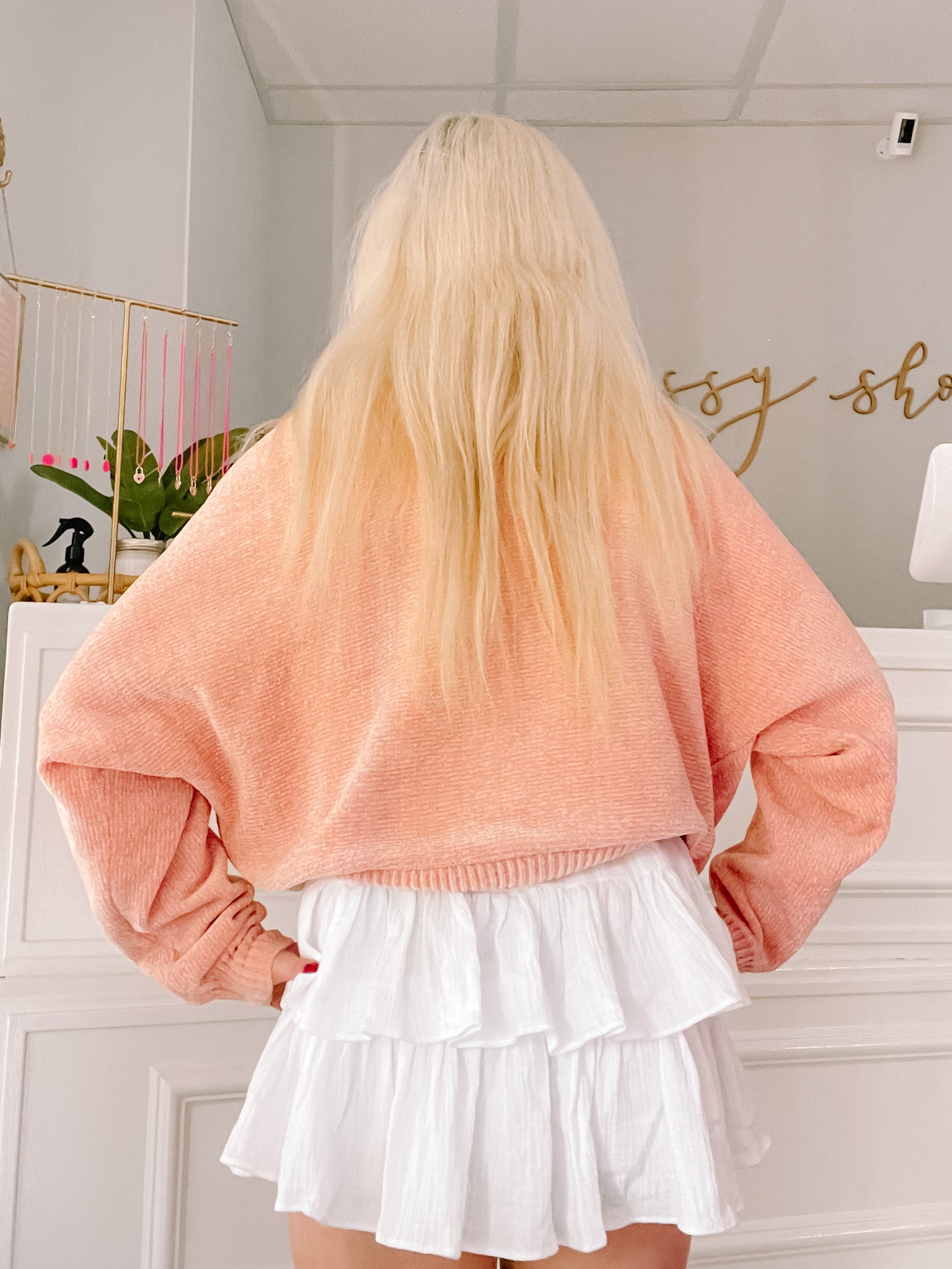 Peach-colored ribbed knit sweater paired with a white tiered mini skirt; rear view.
