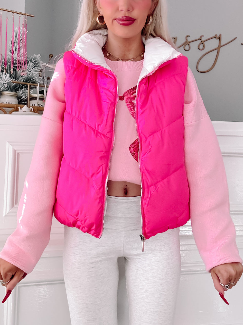 Hot pink puffer vest with a white collar, modeled over a pink sweater and gray leggings.

