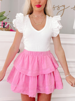 Pink tiered mini skirt with delicate lace trim, styled with a white ruffled top.
