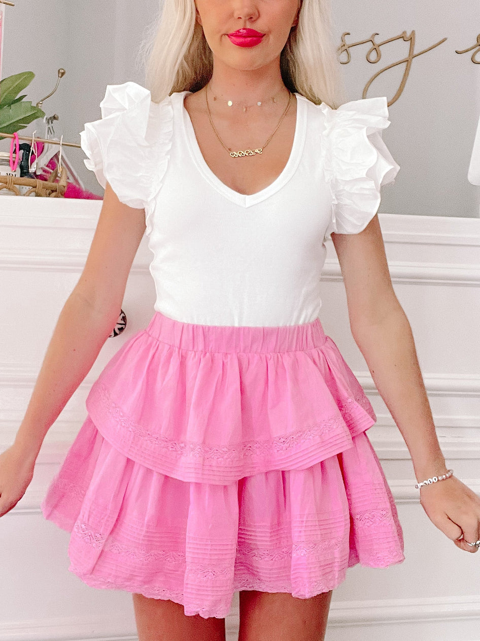 Pink tiered mini skirt with delicate lace trim, styled with a white ruffled top.
