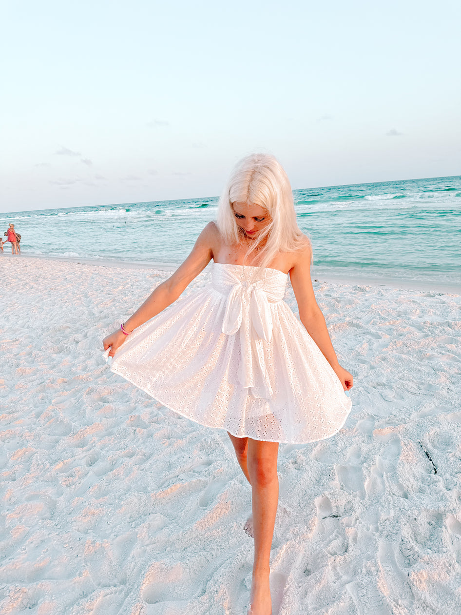 White eyelet mini dress on a beach at sunset.
