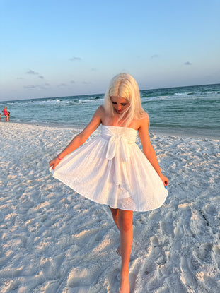 White eyelet mini dress on a beach at sunset.
