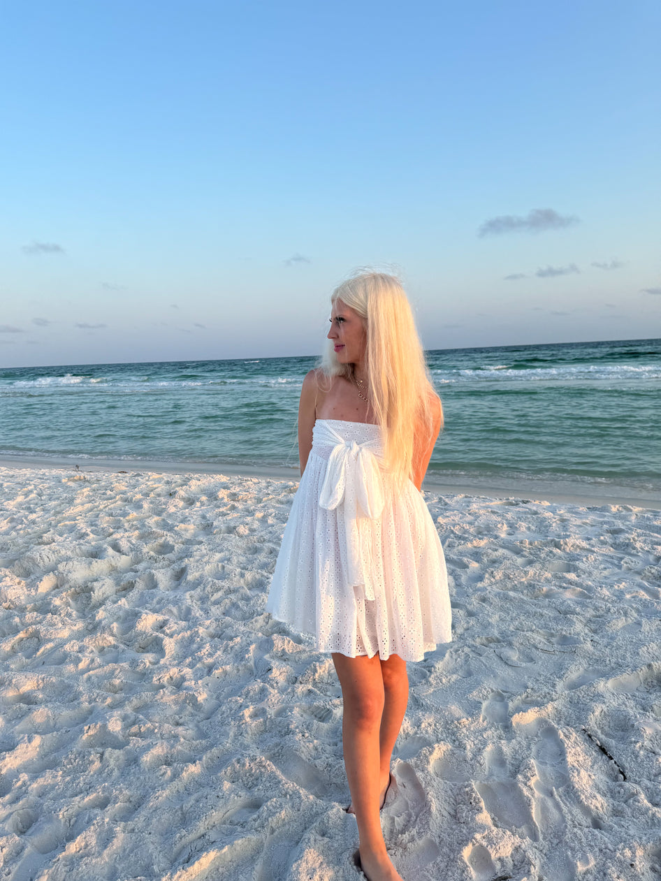 White eyelet mini dress on a beach at sunset.
