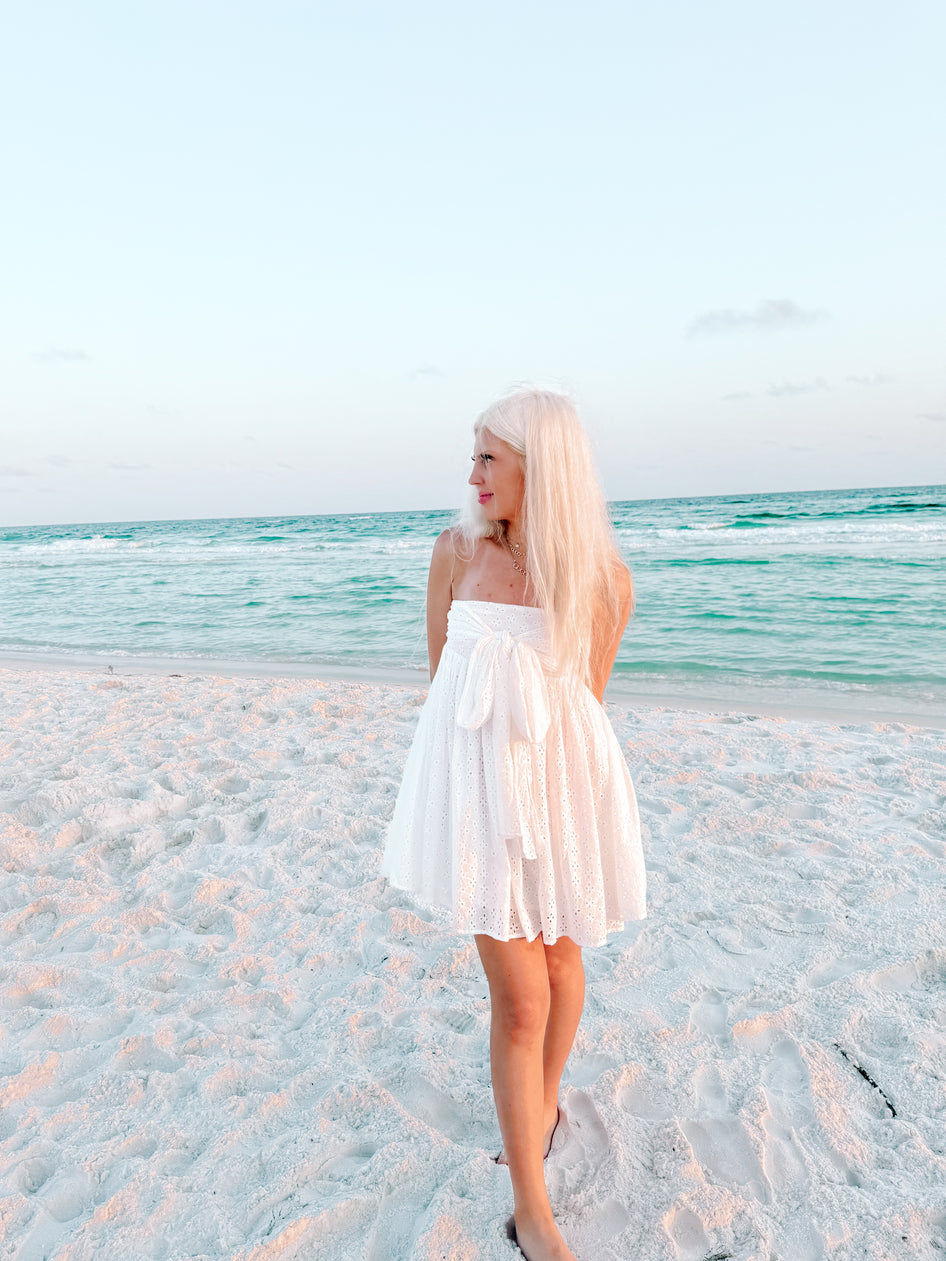 White eyelet mini dress on a beach at sunset.

