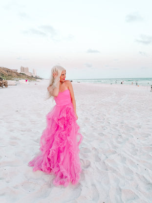 Pink tulle maxi dress with ruffles, on a beach at sunset.
