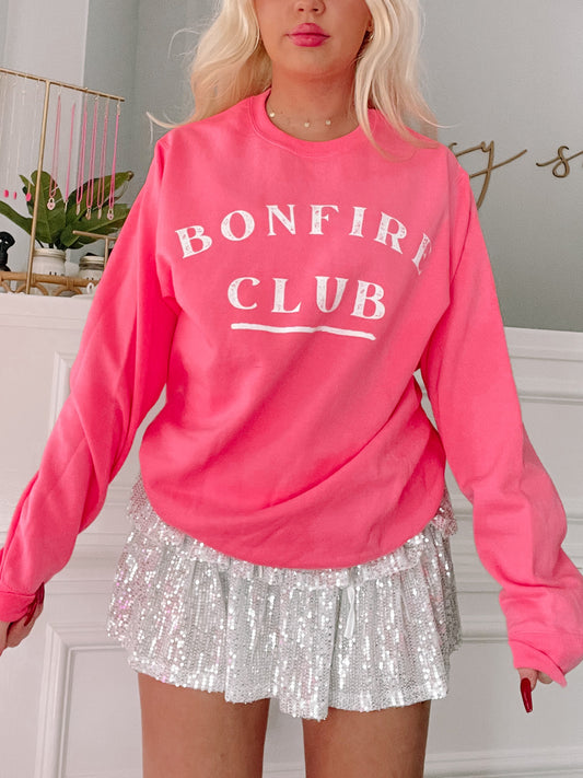 Hot pink crewneck sweatshirt with white "Bonfire Club" lettering; styled with a sparkly skirt.