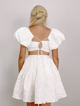 White textured mini dress with puff sleeves and a tie back detail.
