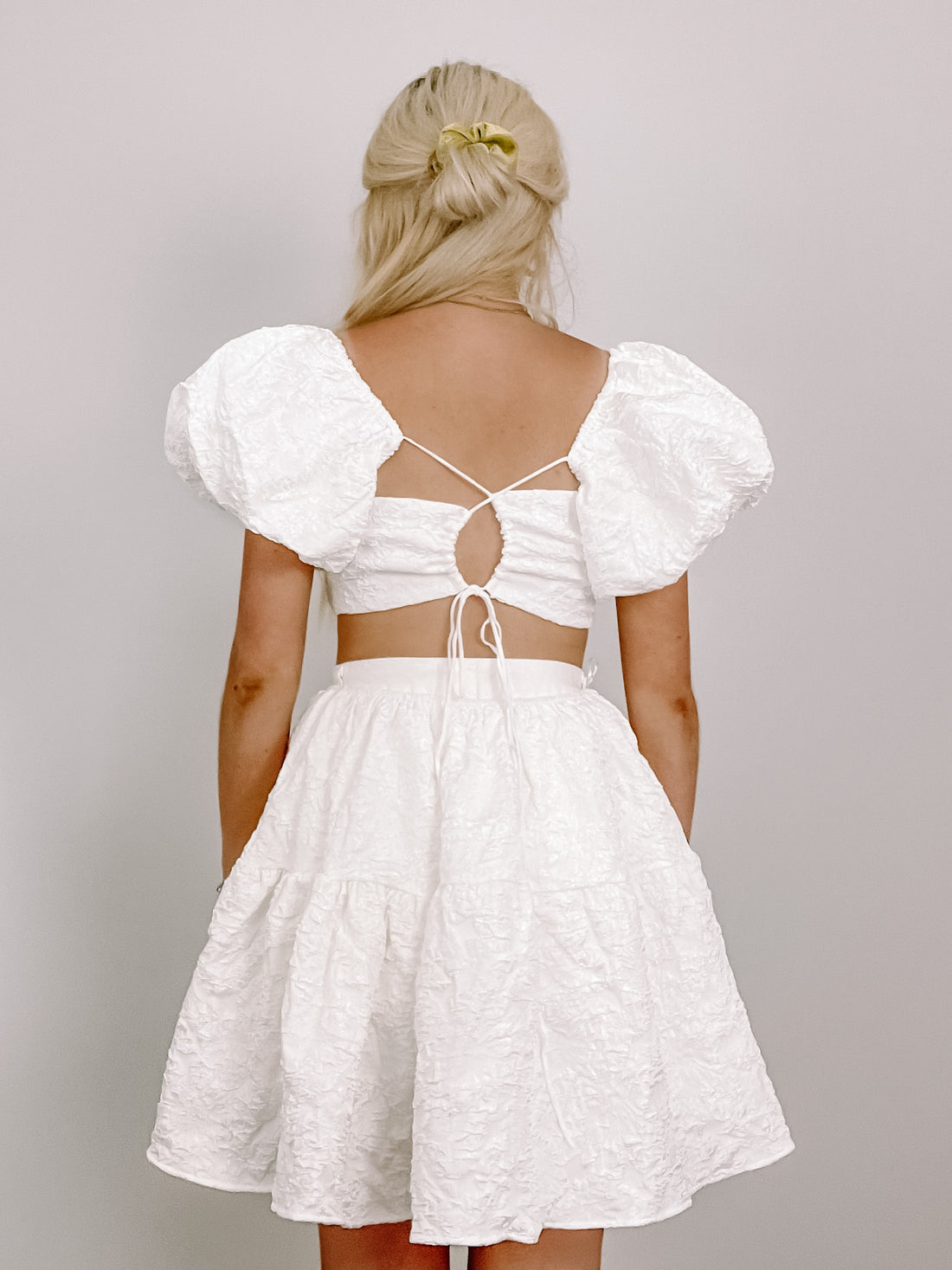 White textured mini dress with puff sleeves and a tie back detail.
