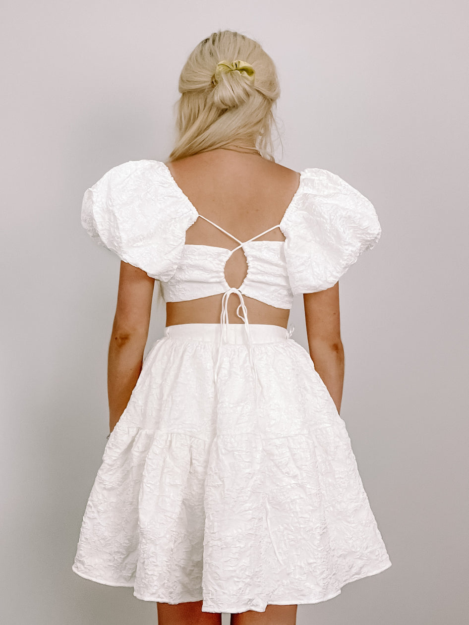 White textured mini dress with puff sleeves and a tie back detail.
