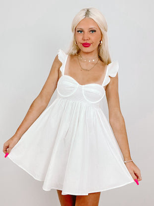 White eyelet mini dress with ruffle straps, modeled against a light background.
