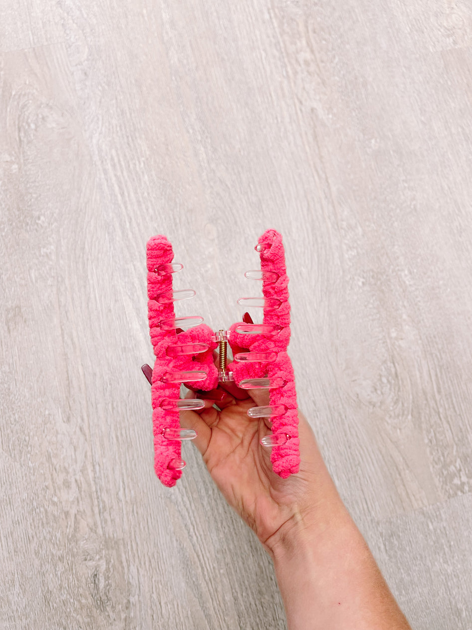 Pink fuzzy claw hair clip held in hand against light wood background.
