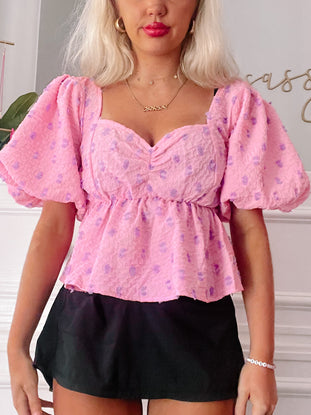 Pink puff-sleeve top with purple floral print, worn with a black mini skirt.
