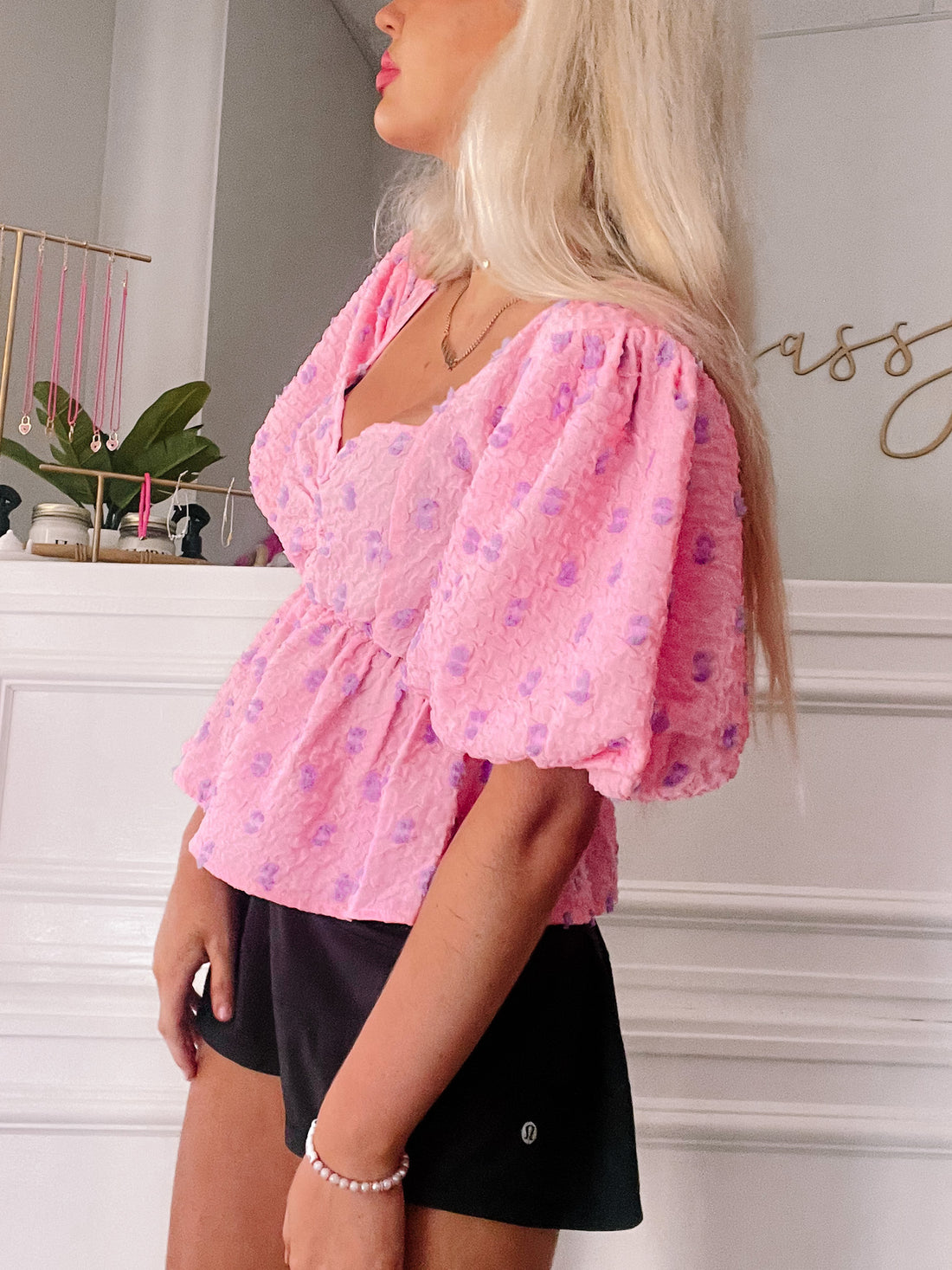 Pink floral puff-sleeve top with a fitted bodice and peplum hem, worn with black shorts.
