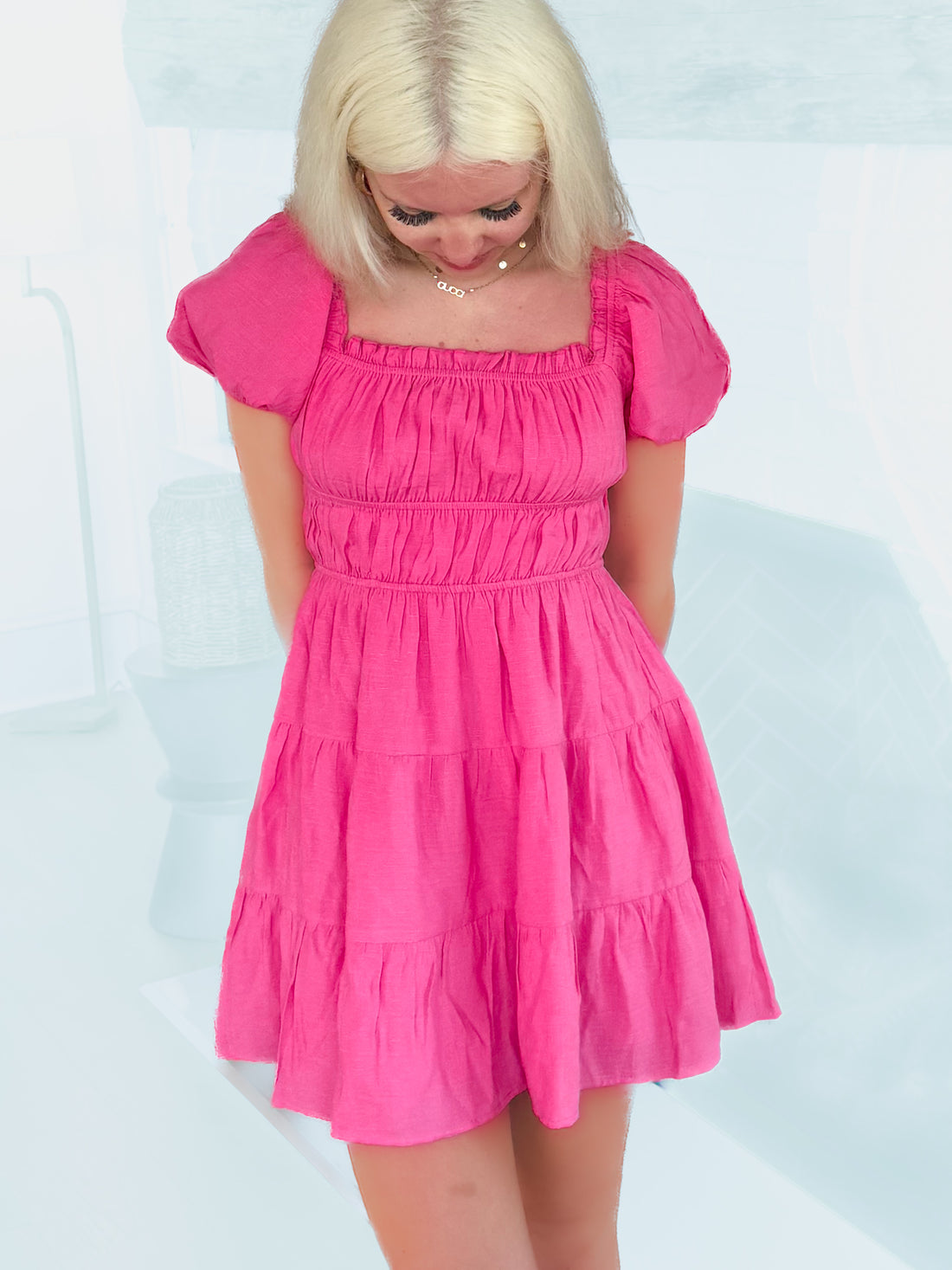 Hot pink tiered mini dress with puff sleeves, shown on model against a light blue background.

