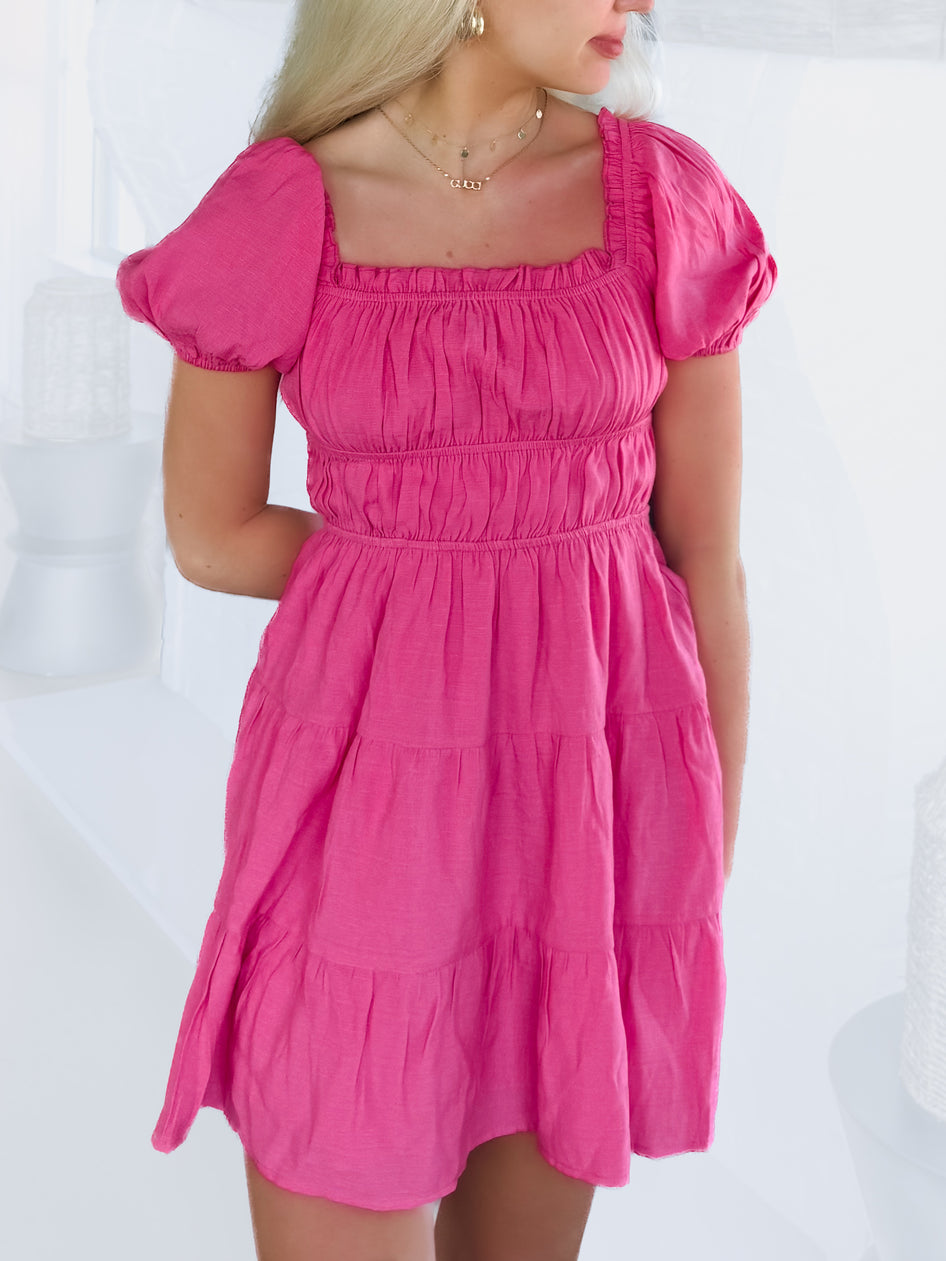 Hot pink tiered mini dress with puff sleeves, shown on a model against a white background.
