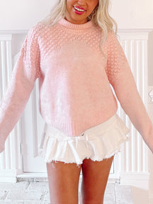 Soft pink sweater with textured detailing, worn indoors.
