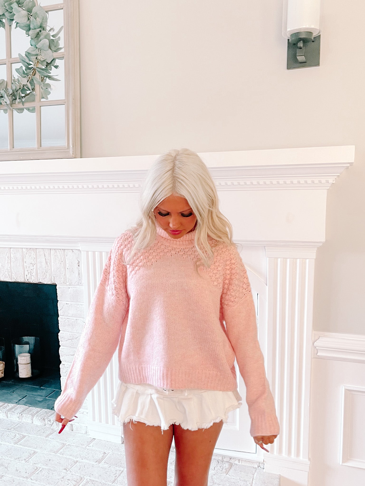 Pink knit sweater styled in a home setting, worn with white shorts.
