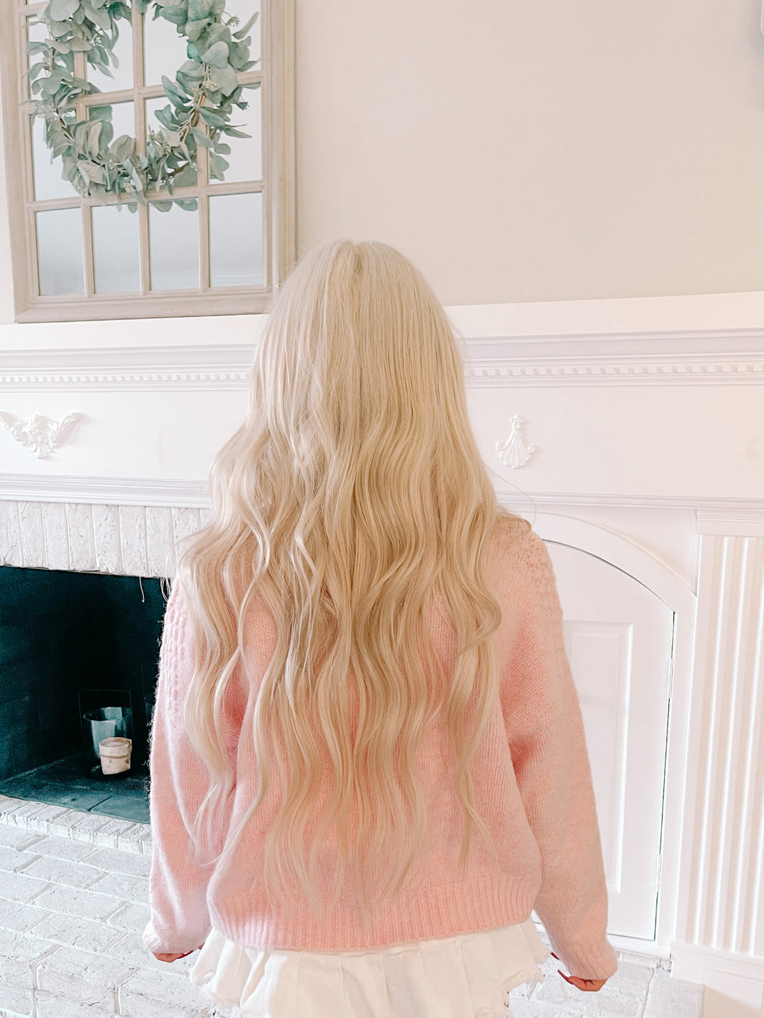 Pink knit sweater shown from behind, worn in a bright living room.
