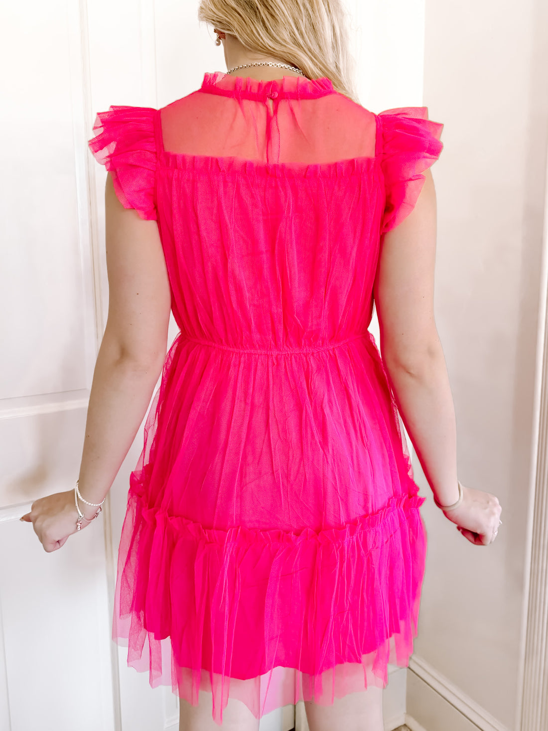 Hot pink mini dress with ruffled trim and sheer mesh overlay, shown from the back.
