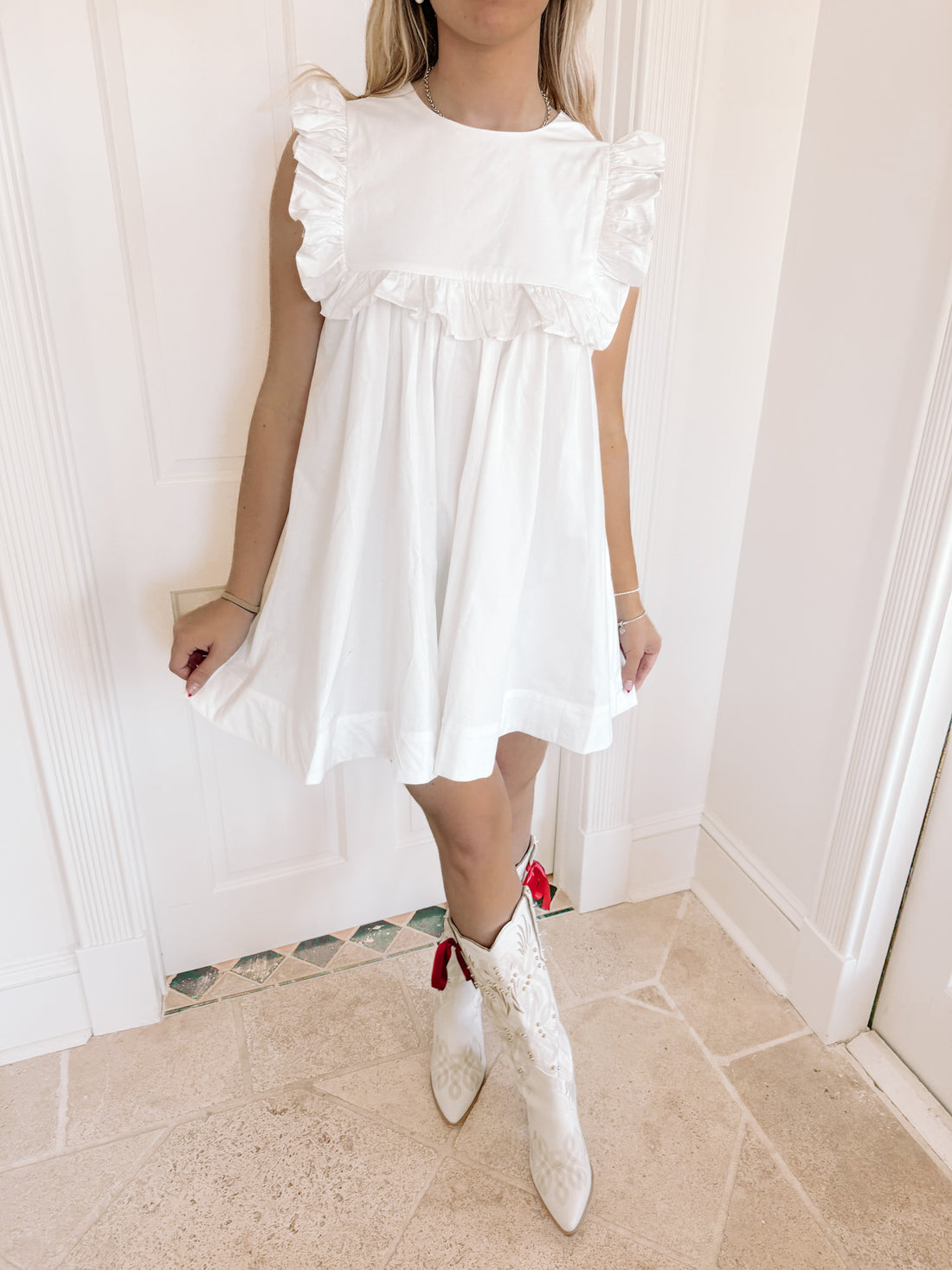 White eyelet mini dress with ruffle detailing, shown on model indoors.
