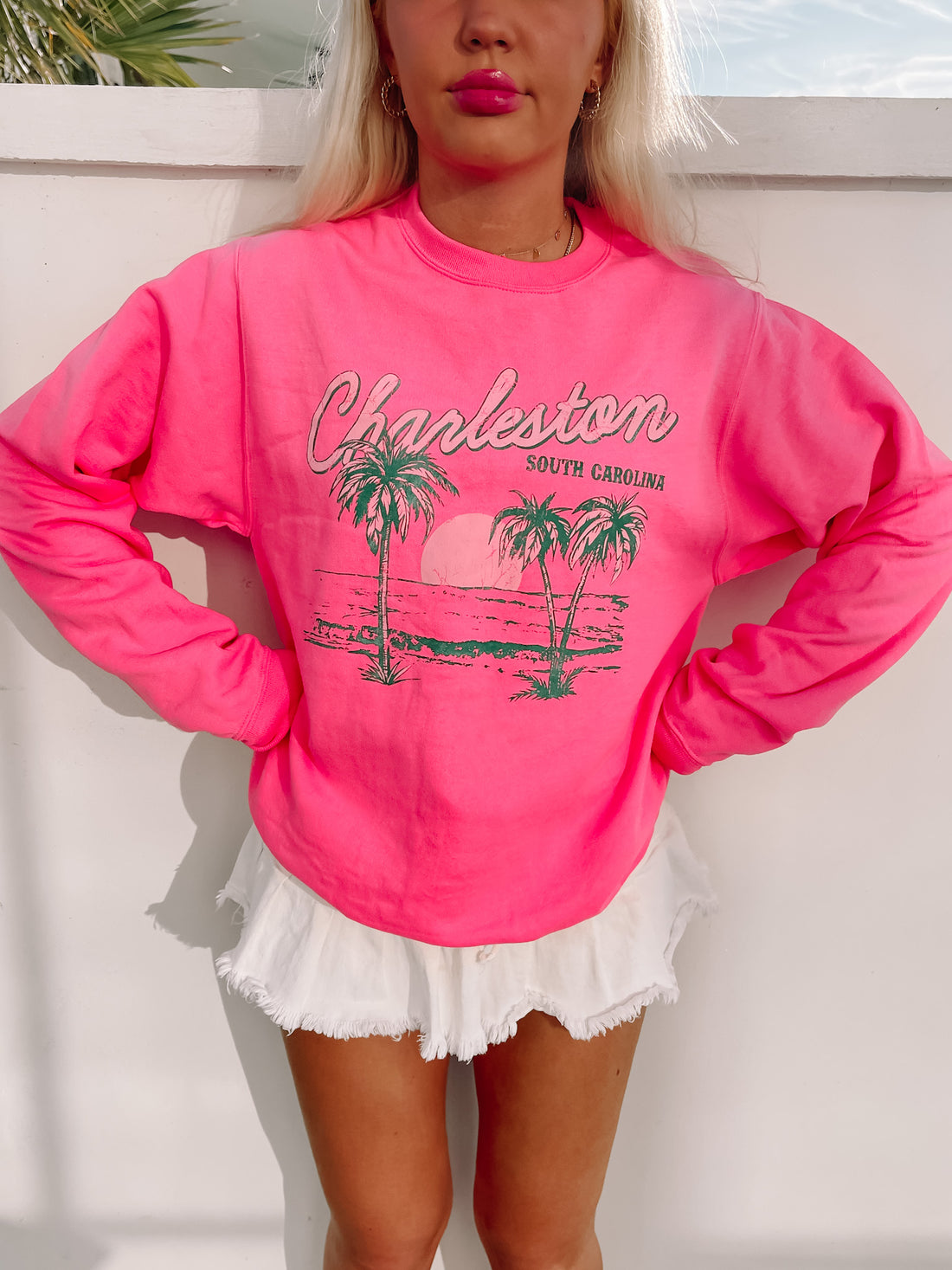 Hot pink crewneck sweatshirt with a palm tree graphic, styled with white shorts.
